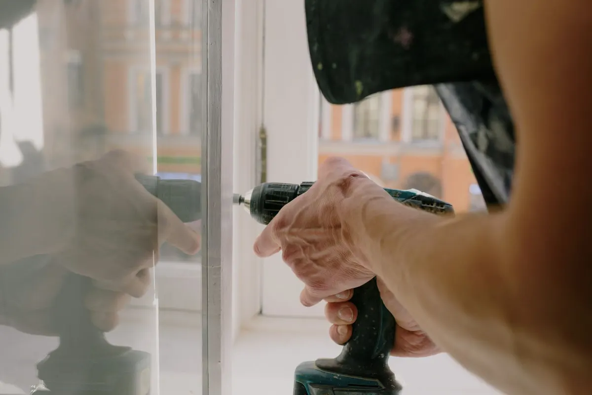 Installer fixing a new white window frame in place with a cordless drill